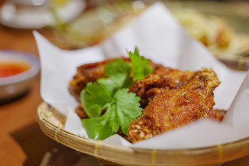 Thai style deep fried crispy chicken wing, on top with cilantro, serve on paper and basket and Sriracha Sauce on side. Thai famous appetizer dish. 