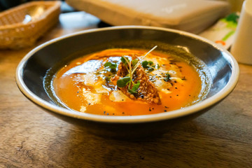 orange thick pumpkin soup in a brown clay plate on a dark wooden table, the dish is decorated with croutons and fresh herbs, a delicious background for the menu                               