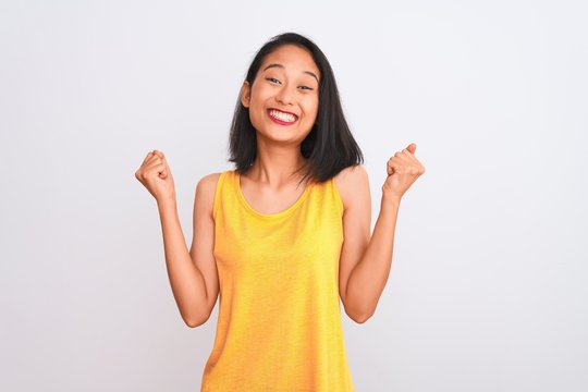 Young chinese woman wearing yellow casual t-shirt standing over isolated white background celebrating surprised and amazed for success with arms raised and open eyes. Winner concept.