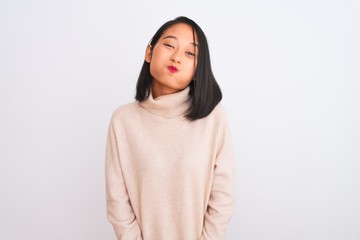 Fototapeta premium Young chinese woman wearing turtleneck sweater standing over isolated white background puffing cheeks with funny face. Mouth inflated with air, crazy expression.