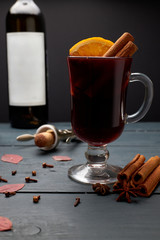 Glass of mulled wine, bottle of red wine and corkscrew with open cork on wooden table. Hot red wine with various spices.