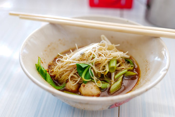 Close up view of Spicy Thai Boat rice Noodle Soup,  Kuai Tiao Ruea, serve on ceramic bowl on white wooden table. 