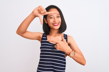 Obraz na płótnie Canvas Young chinese woman wearing striped t-shirt standing over isolated white background smiling making frame with hands and fingers with happy face. Creativity and photography concept.