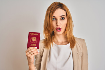 Redhead caucasian business woman holding passport of Russia over isolated background scared in shock with a surprise face, afraid and excited with fear expression