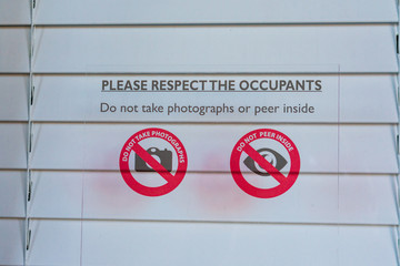 Sign prohibiting taking pictures and peering inside of the window with closed shutters notifies...