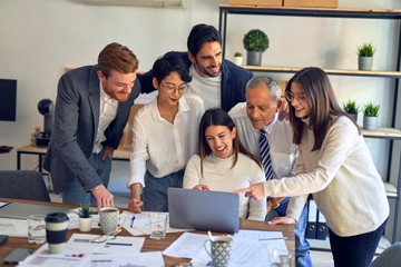 Group of business workers smiling happy and confident. One of them sitting and partners standing around. Working together with smile on face looking at the laptop at the office