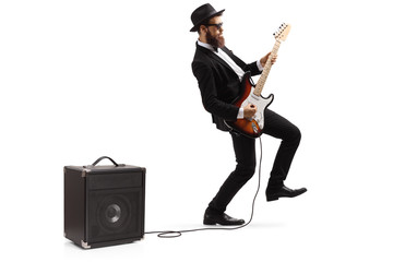 Bearded male artist in a suit playing a plugged electric guitar