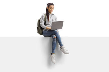 Female student sitting on a blank board and using a laptop computer - Powered by Adobe