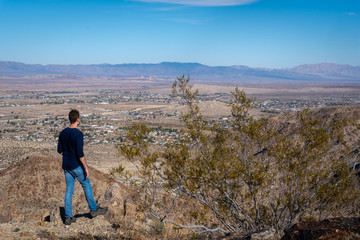 Hiker standing on cliff edge looking down at desert town and vast valley landscape