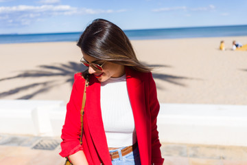 Young beautiful woman walking down the promenade by the beach, smiling and enjoying a sunny day