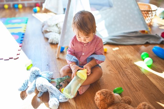 Adorable toddler holding feeding bottle around lots of toys at kindergarten