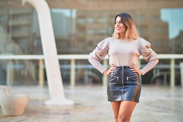 Young beautiful woman wearing sweater and skirt smiling happy and confident. Standing with smile on face at the town street