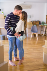 Fototapeta na wymiar Young beautiful couple hugging and kissing at new home around cardboard boxes
