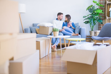 Young beautiful couple sitting on the sofa at new home around cardboard boxes