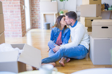Young beautiful couple sitting on the floor kissing at new home around cardboard boxes