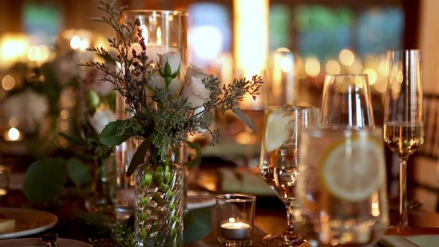 Wedding event interior table setting details decorated with champagne flutes candles white roses flowers in glass vases filled with water