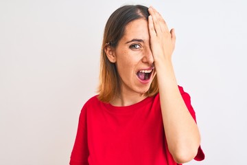 Beautiful redhead woman wearing casual red t-shirt over isolated background covering one eye with hand, confident smile on face and surprise emotion.