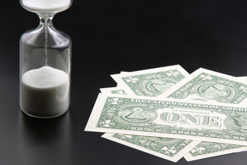 Dollar bills lie near the hourglass. Time is money. The salary. Business solutions in time. Hourglass time measurement