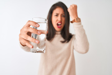 Young beautiful chinese woman holding glass of water standing over isolated white background annoyed and frustrated shouting with anger, crazy and yelling with raised hand, anger concept