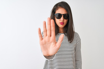 Chinese woman wearing striped t-shirt and sunglasses standing over isolated white background doing stop sing with palm of the hand. Warning expression with negative and serious gesture on the face.