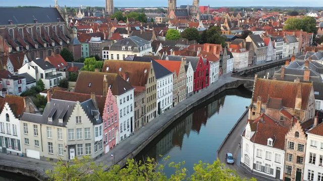 Aerial pan up reveal from building reflections in Bruges canals to find the historic Belfry bell tower and other landmarks which dominate the pretty city.