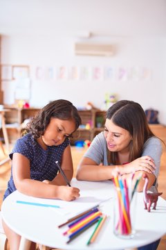 Beautiful teacher and toddler girl drawing draw using colored pencils at kindergarten
