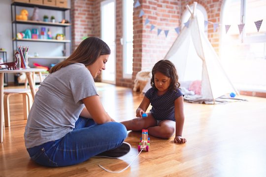 Beautiful teacher and toddler girl playing with train at kindergarten