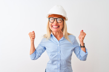 Middle age architect woman wearing glasses and helmet over isolated white background very happy and excited doing winner gesture with arms raised, smiling and screaming for success. Celebration