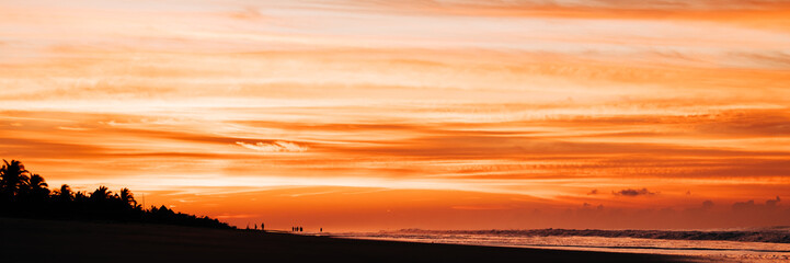 Naklejka premium Panoramic shot showing silhouettes of people waiting for the sunrise at the beach.