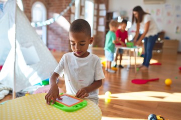 Fototapeta premium Young beautiful teacher and toddlers playing around lots of toys at kindergarten