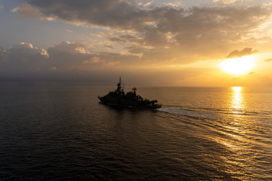 Silhouette of warship sails in the sea with golden light brace upon the sea surface.