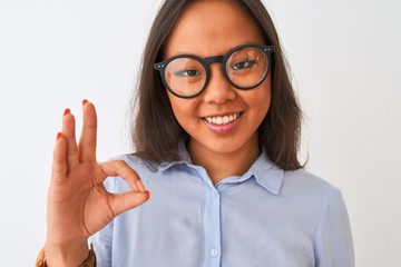 Young chinese woman wearing shirt and glasses standing over isolated white background doing ok sign with fingers, excellent symbol