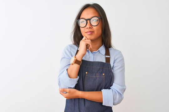 Young beautiful chinese woman wearing glasses and apron over isolated white background with hand on chin thinking about question, pensive expression. Smiling with thoughtful face. Doubt concept. - Powered by Adobe