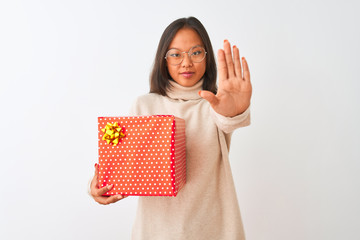 Young chinese woman wearing glasses holding birthday gift over isolated white background with open hand doing stop sign with serious and confident expression, defense gesture