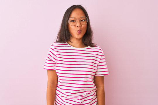 Young chinese woman wearing striped t-shirt and glasses over isolated pink background making fish face with lips, crazy and comical gesture. Funny expression.