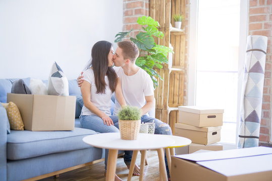 Young beautiful couple sitting on the sofa drinking coffee at new home around cardboard boxes