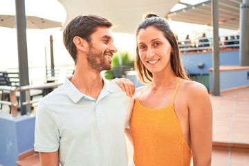 Young beautiful couple on vacation smiling happy and confident. Standing with smile on face hugging at the beach