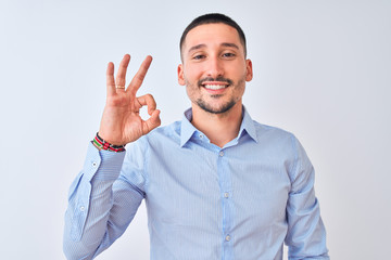 Young handsome business man standing over isolated background smiling positive doing ok sign with hand and fingers. Successful expression.