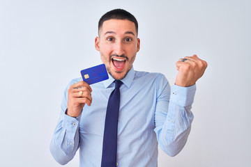 Young business man holding credit card over isolated background screaming proud and celebrating victory and success very excited, cheering emotion