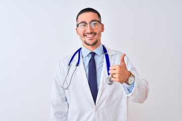 Young doctor man wearing stethoscope over isolated background doing happy thumbs up gesture with hand. Approving expression looking at the camera showing success.