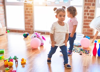 Fototapeta premium Adorable toddlers standing around lots of toys at kindergarten