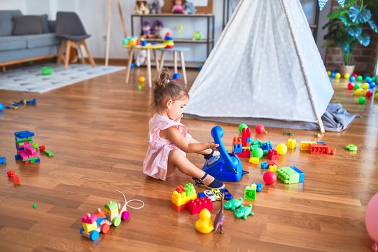 Young beautiful toddler sitting on the floor playing with vintage telephone at kindergaten