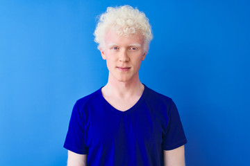 Young albino blond man wearing casual t-shirt standing over isolated blue background with serious expression on face. Simple and natural looking at the camera.