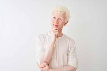 Young albino blond man wearing casual t-shirt standing over isolated white background with hand on chin thinking about question, pensive expression. Smiling with thoughtful face. Doubt concept.