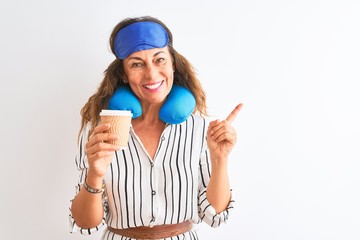 Tourist woman wearing neckpillow sleep mask drinking coffee over isolated white background very happy pointing with hand and finger to the side