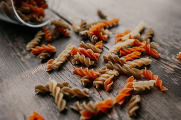 multi-colored raw spiral pasta, orange and yellow, scattered from a glass jar on a dark wooden floor