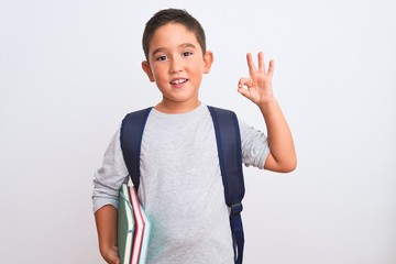 Beautiful student kid boy wearing backpack holding books over isolated white background doing ok sign with fingers, excellent symbol