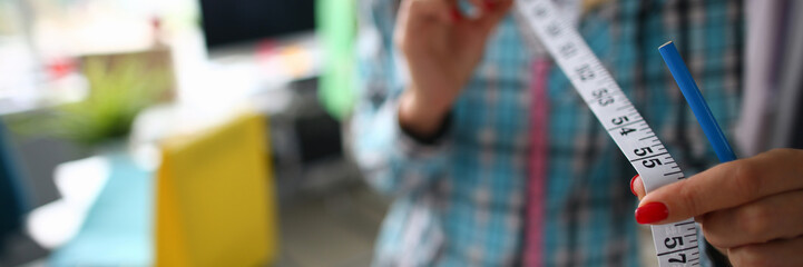 Focus on tender female hands holding important measuring utility and wearing fashionable clothes. Witty girl working on significant project. Fashioner workshop concept . Blurred background