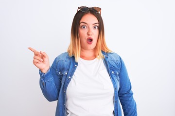 Beautiful woman wearing denim shirt standing over isolated white background Surprised pointing with finger to the side, open mouth amazed expression.