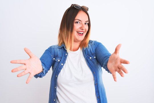 Beautiful woman wearing denim shirt standing over isolated white background looking at the camera smiling with open arms for hug. Cheerful expression embracing happiness.